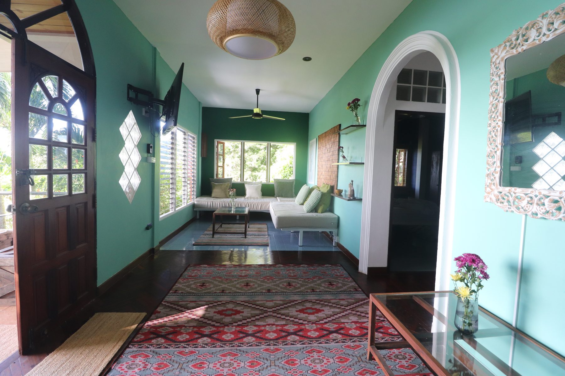 The living room of Sea Breeze villa: green walls, archway, patterned rug, wooden floor, and an open door looking out to the garden